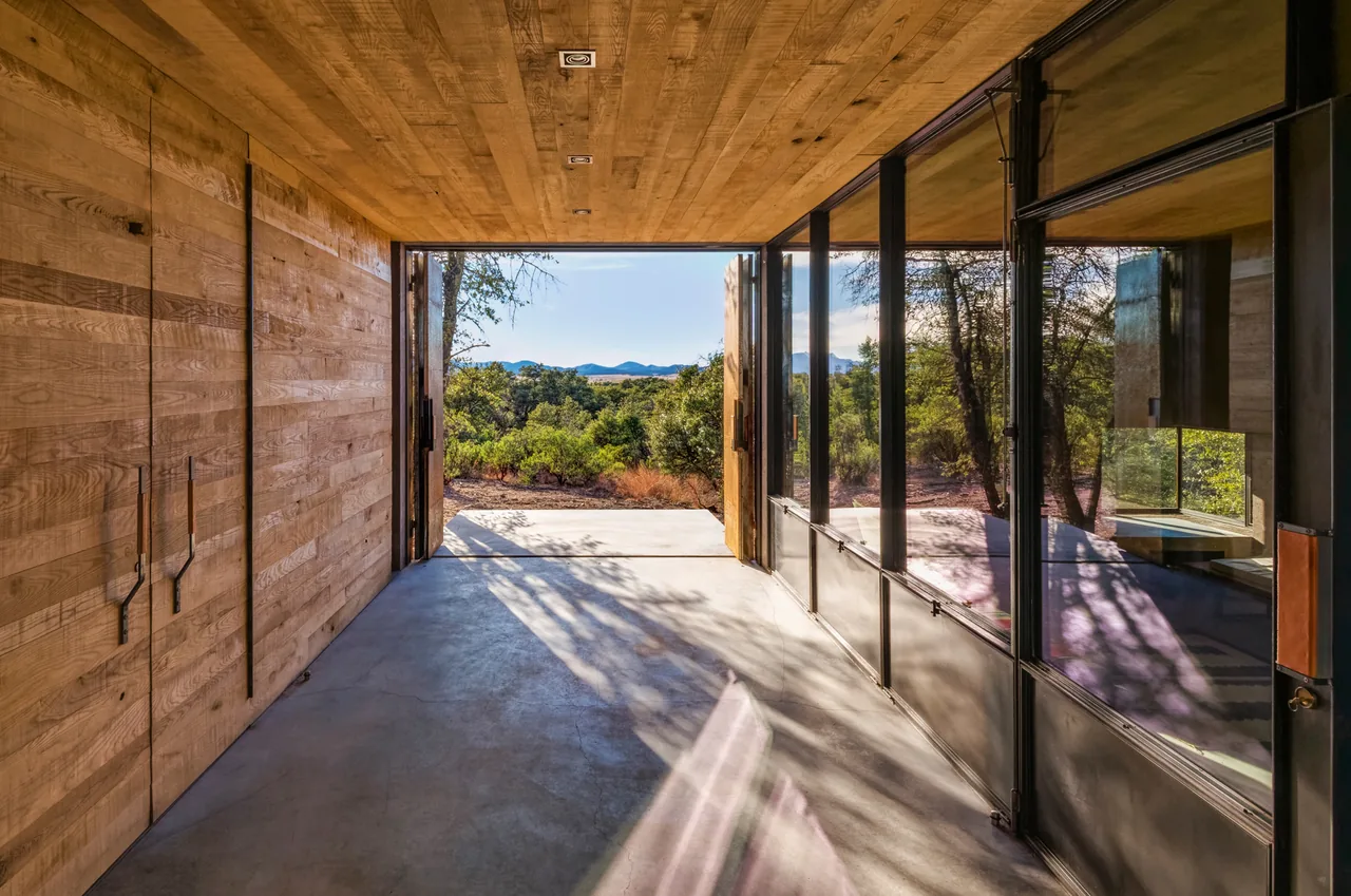 Casa Caldera features a recessed wood-paneled corridor with floor-to-ceiling black steel and glass doors facing nature.