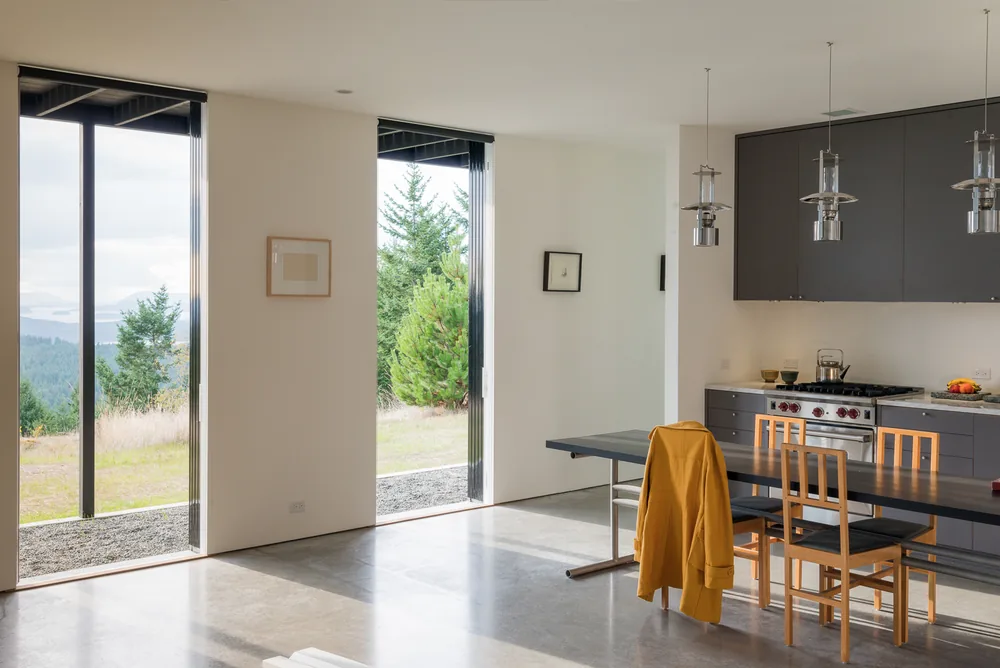 Island Home + Studio kitchen with concrete flooring, floor-to-ceiling glazing, and pendant lighting.
