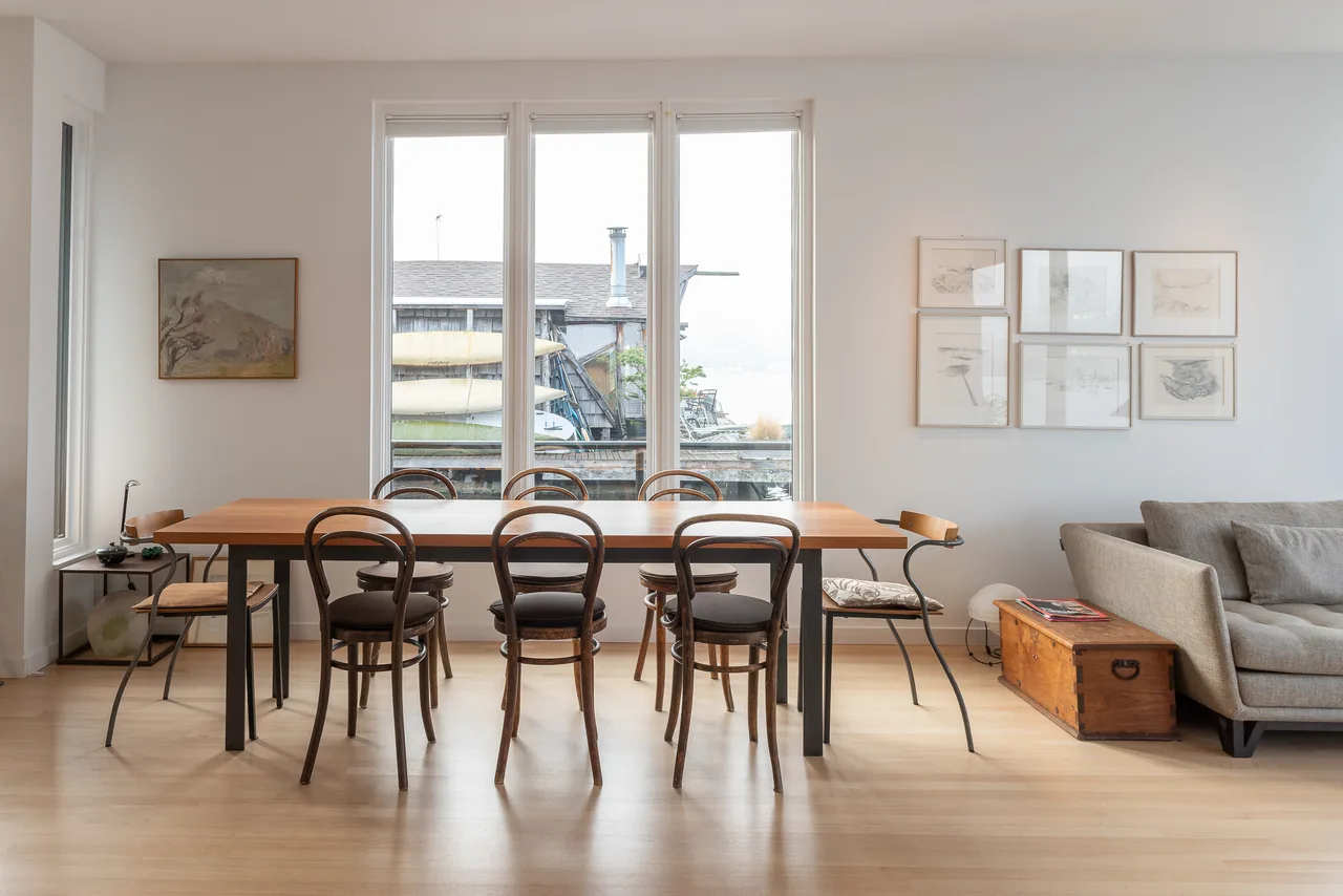 Dining area with wooden table and bentwood chairs in a floating home by Atelier Drome with lake views from large windows.
