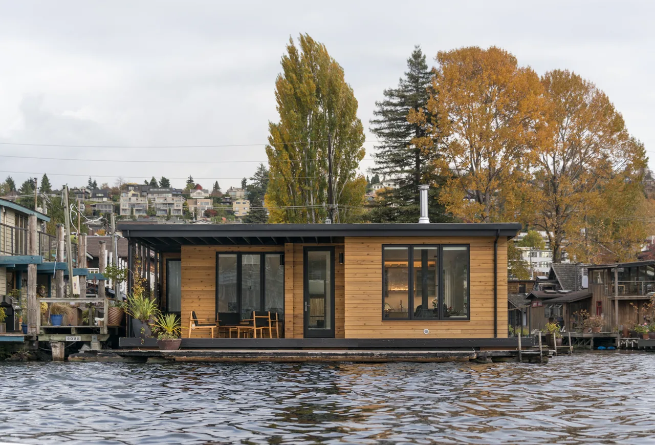 The Lake Union Floating Home features horizontal wood siding, black-framed windows, and a flat roof over a lakeside porch.