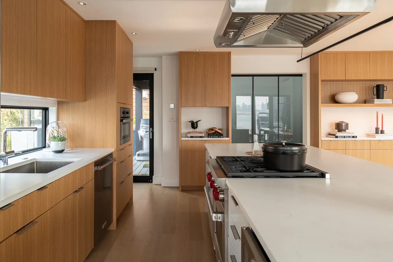 The Ship Canal Floating Home kitchen features wood cabinetry, a large island with gas cooktop, and a view through the rear glass door.