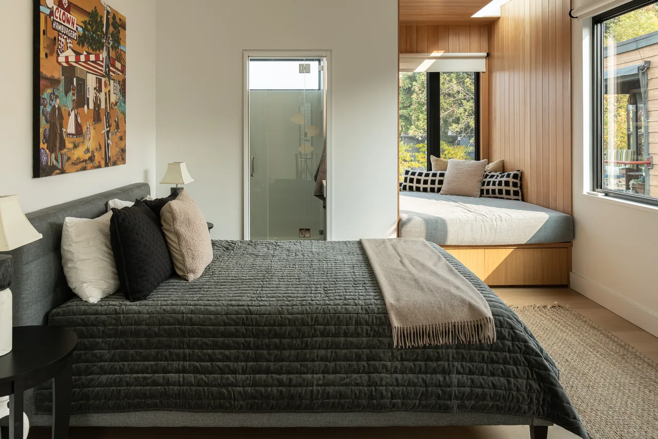 The Ship Canal Floating Home bedroom features a gray bed, wooden-paneled window seat, and large windows for natural light.