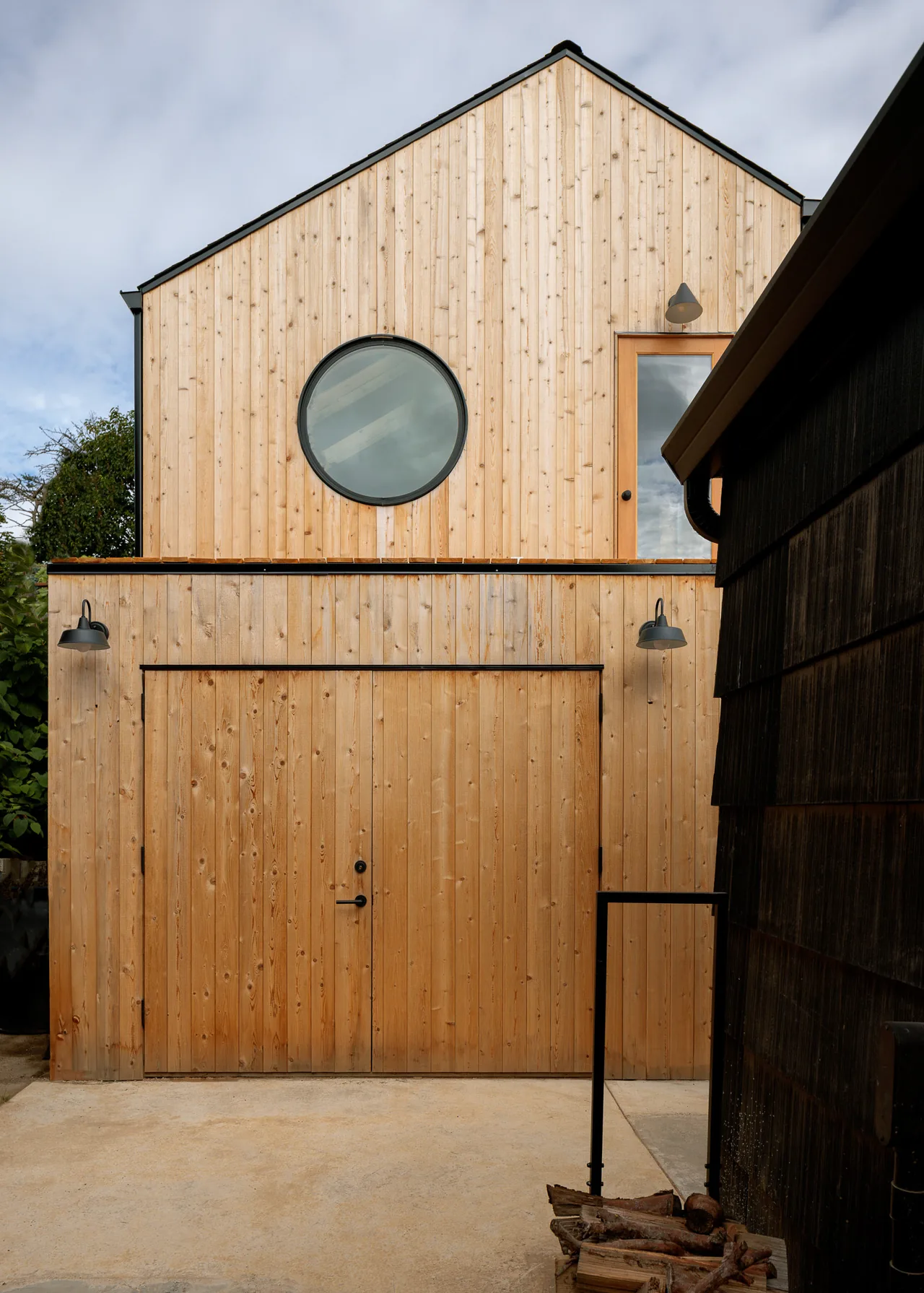 The Moonwave DADU features natural wood paneling with a round window and garage door on its exterior front facade.