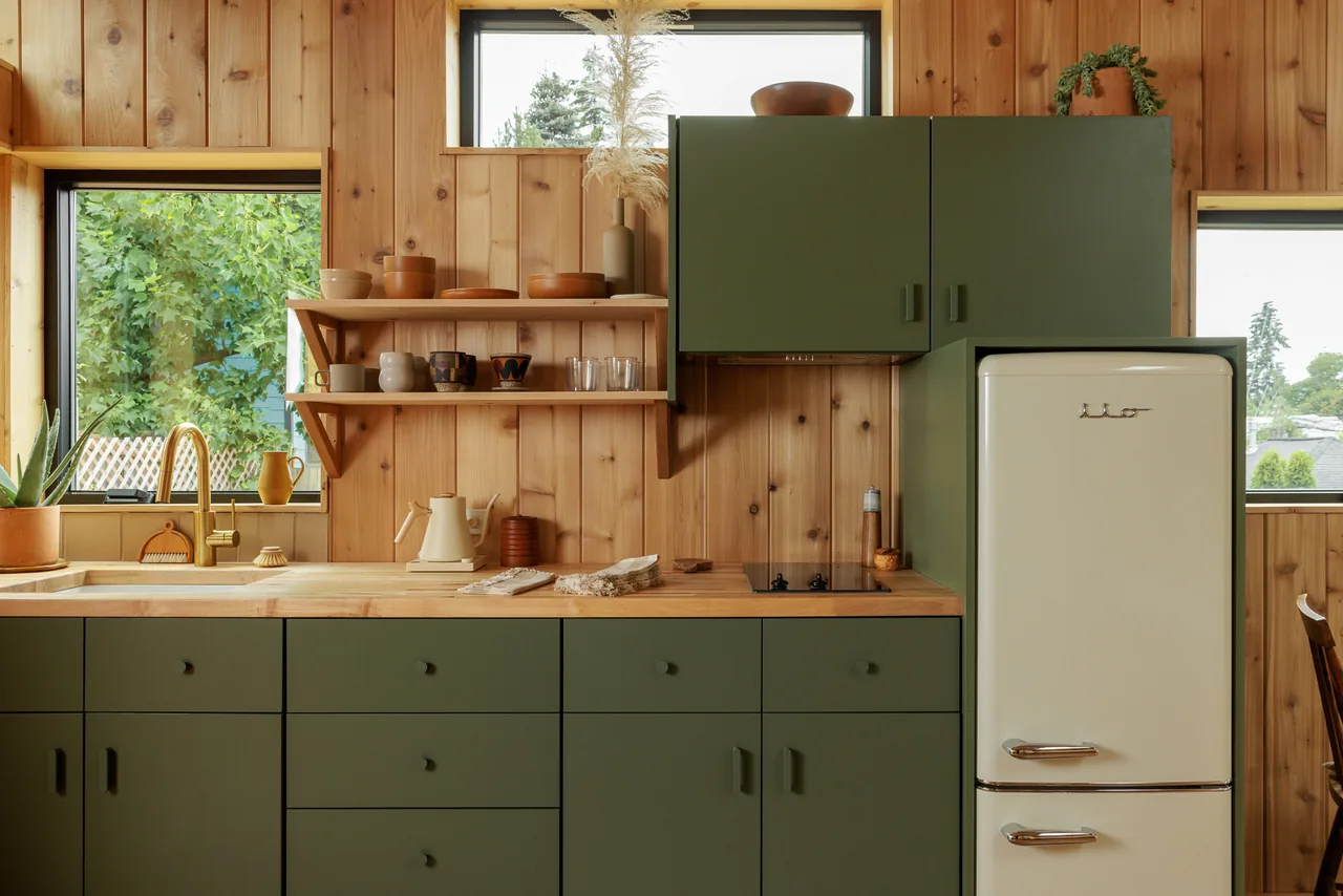 Kitchen with olive green cabinetry, light wood panel walls, and a small white vintage refrigerator.