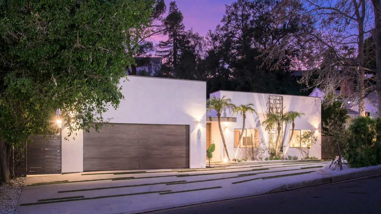 Modern white stucco house with flat roofs and wooden garage door illuminated at dusk.