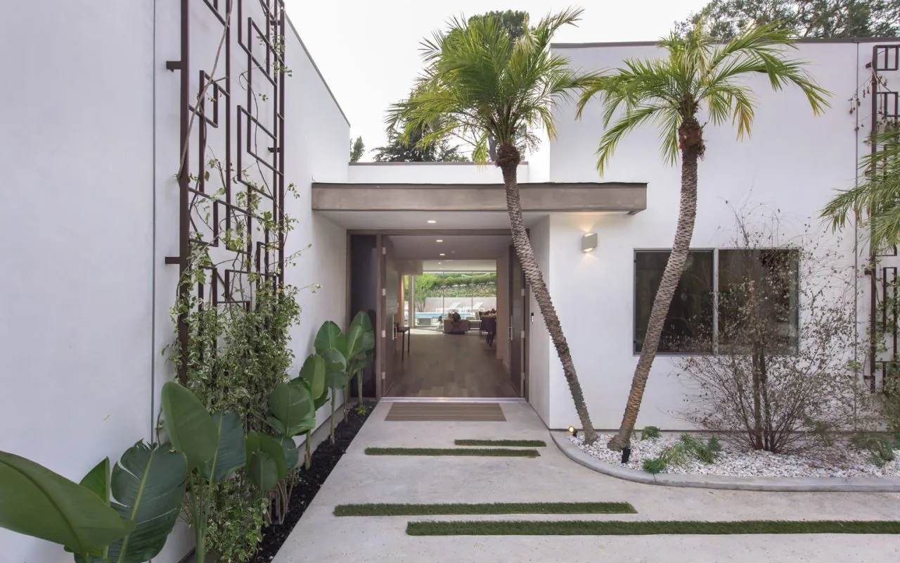 Entrance view of 2213 Roscomare featuring a concrete walkway with grass strips flanked by palm trees and white walls leading indoors.