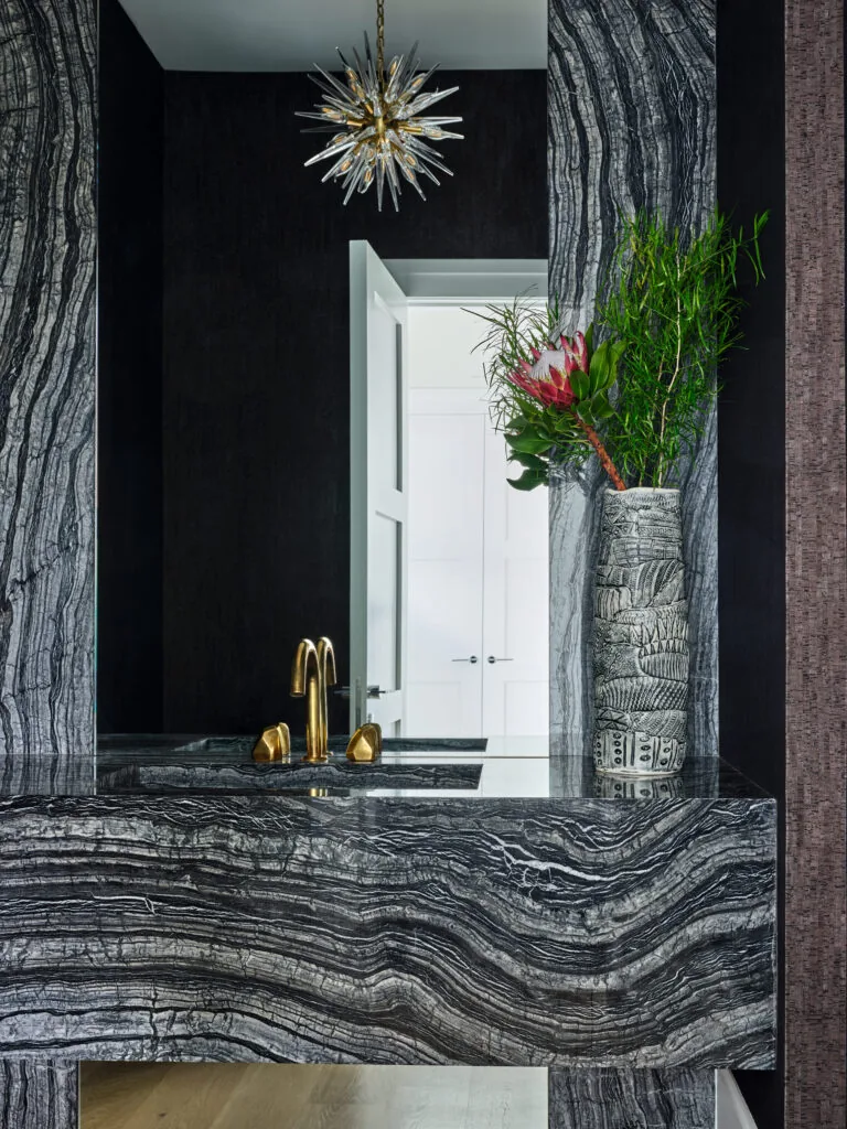 A bathroom vanity with striking black and white stone surfaces, accented by a gold faucet and sculptural light fixture.