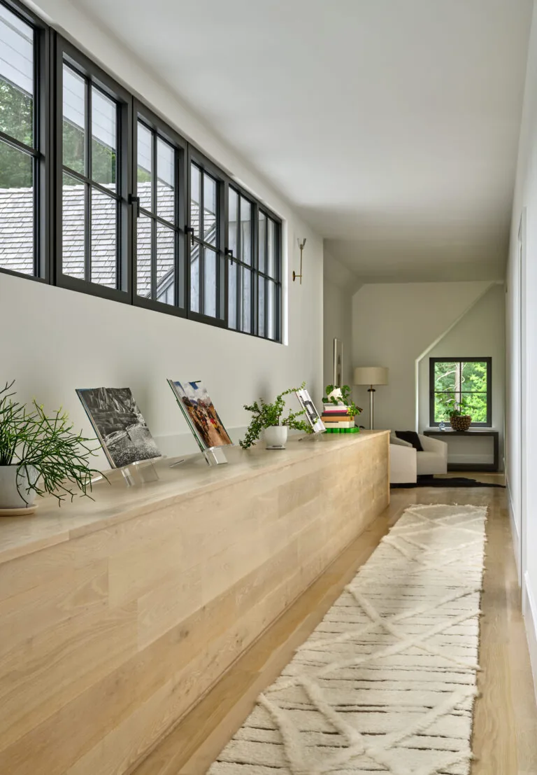 A bright hallway features black window frames and a custom wood cabinet with decorative items on top.