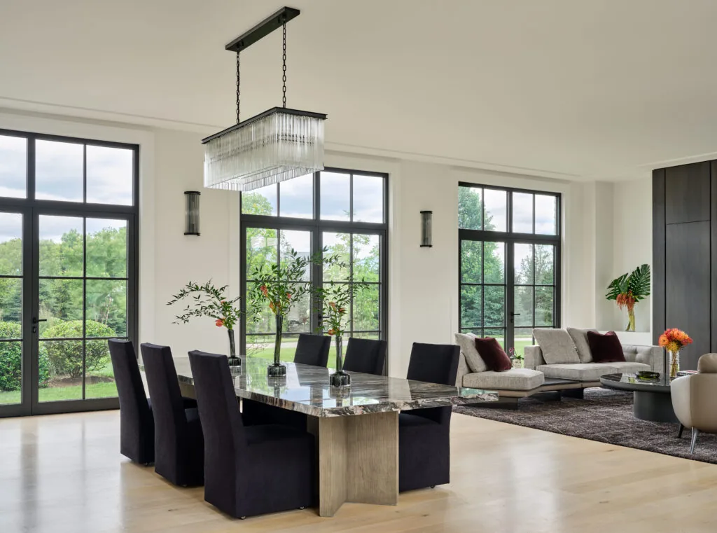 Dining and living area with marble table, black-framed grid windows, and modern furniture in a Bauhaus-style farmhouse.