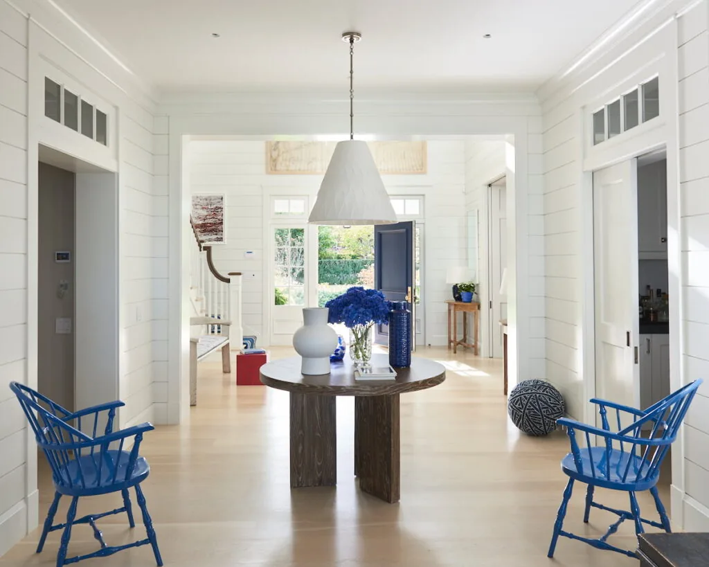 Entryway featuring a round wooden table, blue chairs, and white walls with shiplap paneling.