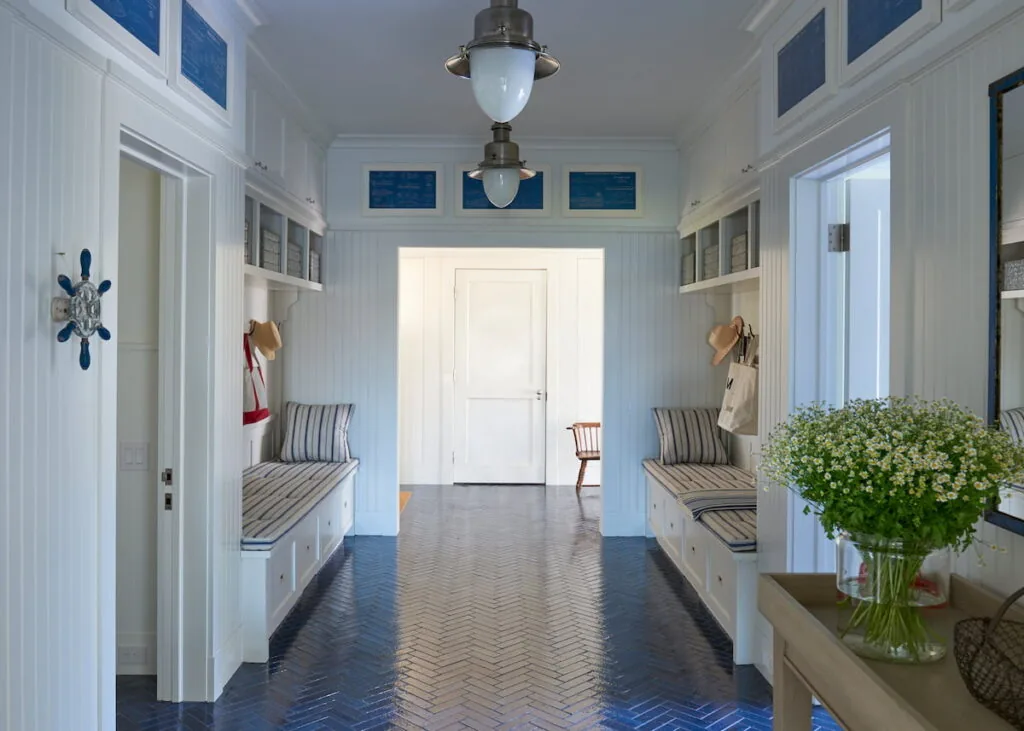 Mudroom hallway with built-in bench seating, beadboard walls, and blue herringbone tile flooring.