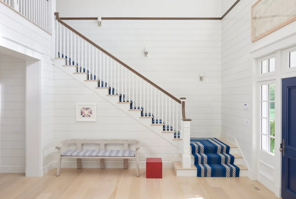 Entry hallway with painted wood panel walls, blue runner on staircase, and light wood flooring.