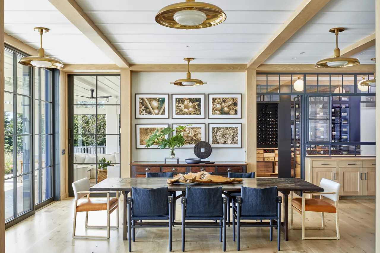 Dining area featuring a wooden table with varied chairs, framed art, and large sliding glass doors connecting to an outdoor space.