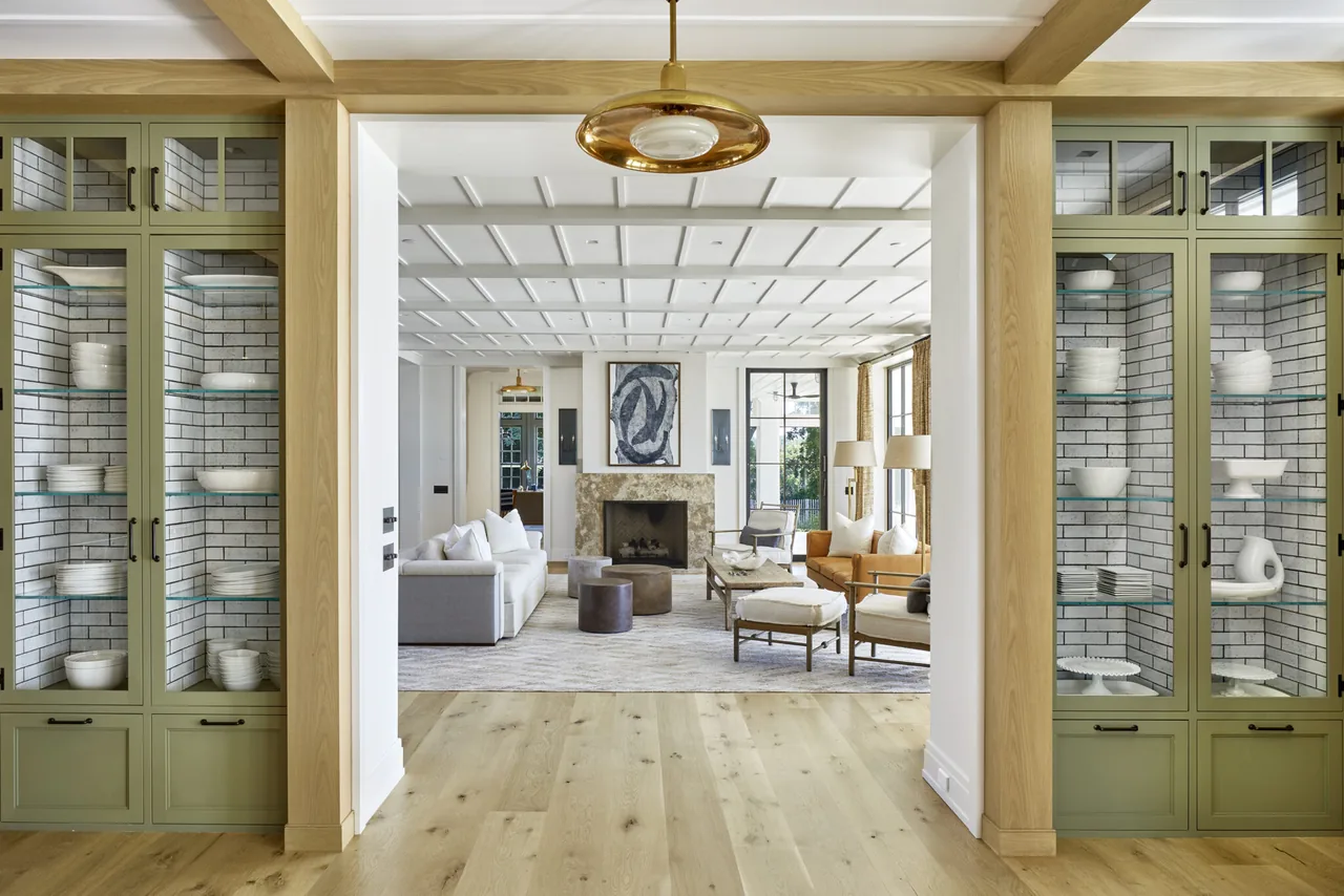 Living room with a central fireplace flanked by gray sectional sofa and wooden armchairs, and built-in glass display cabinets.