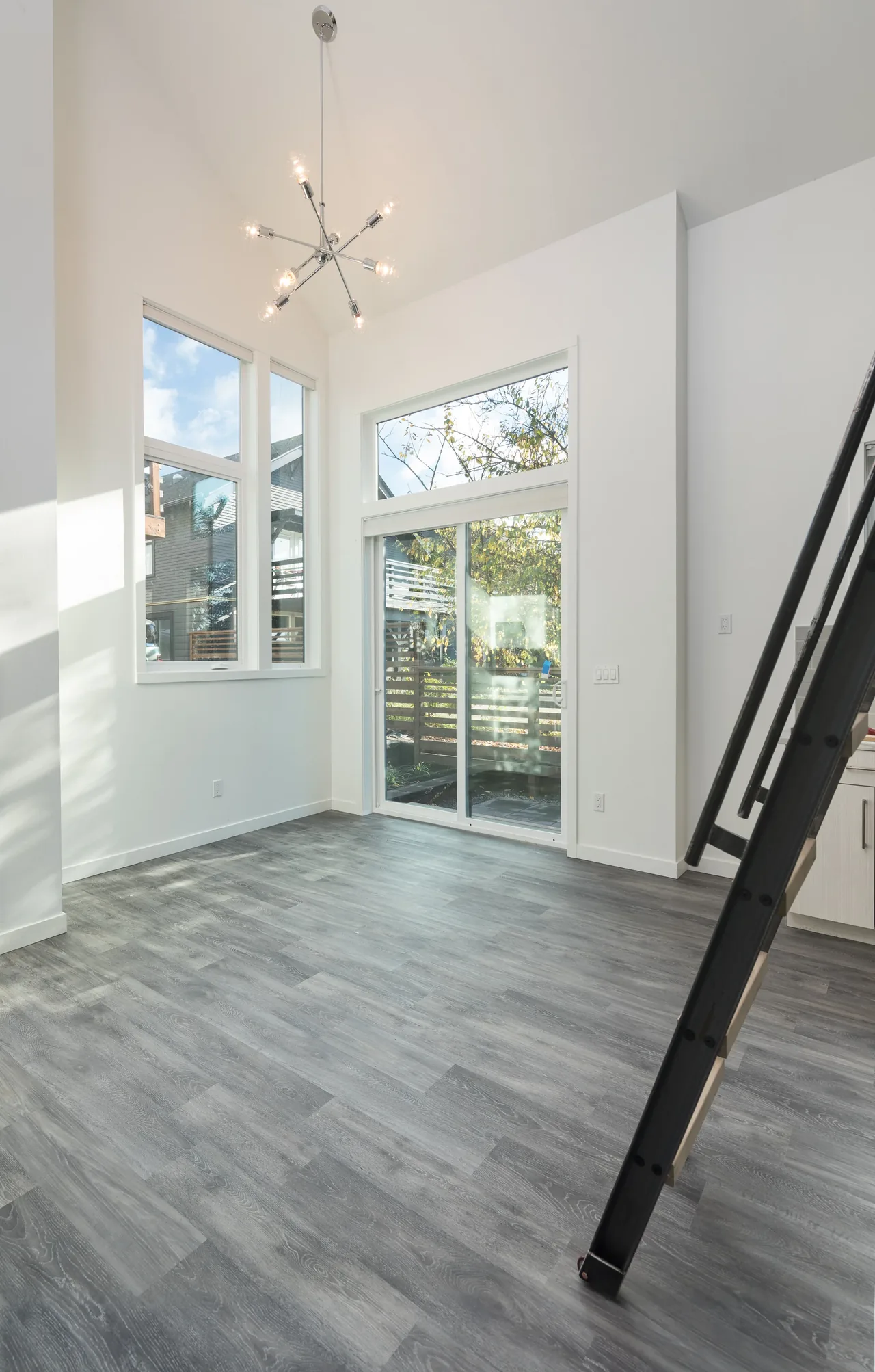 Interior view of a small room with floor-to-ceiling windows, glass sliding door, and a modern chandelier lighting a wood-patterned vinyl floor.