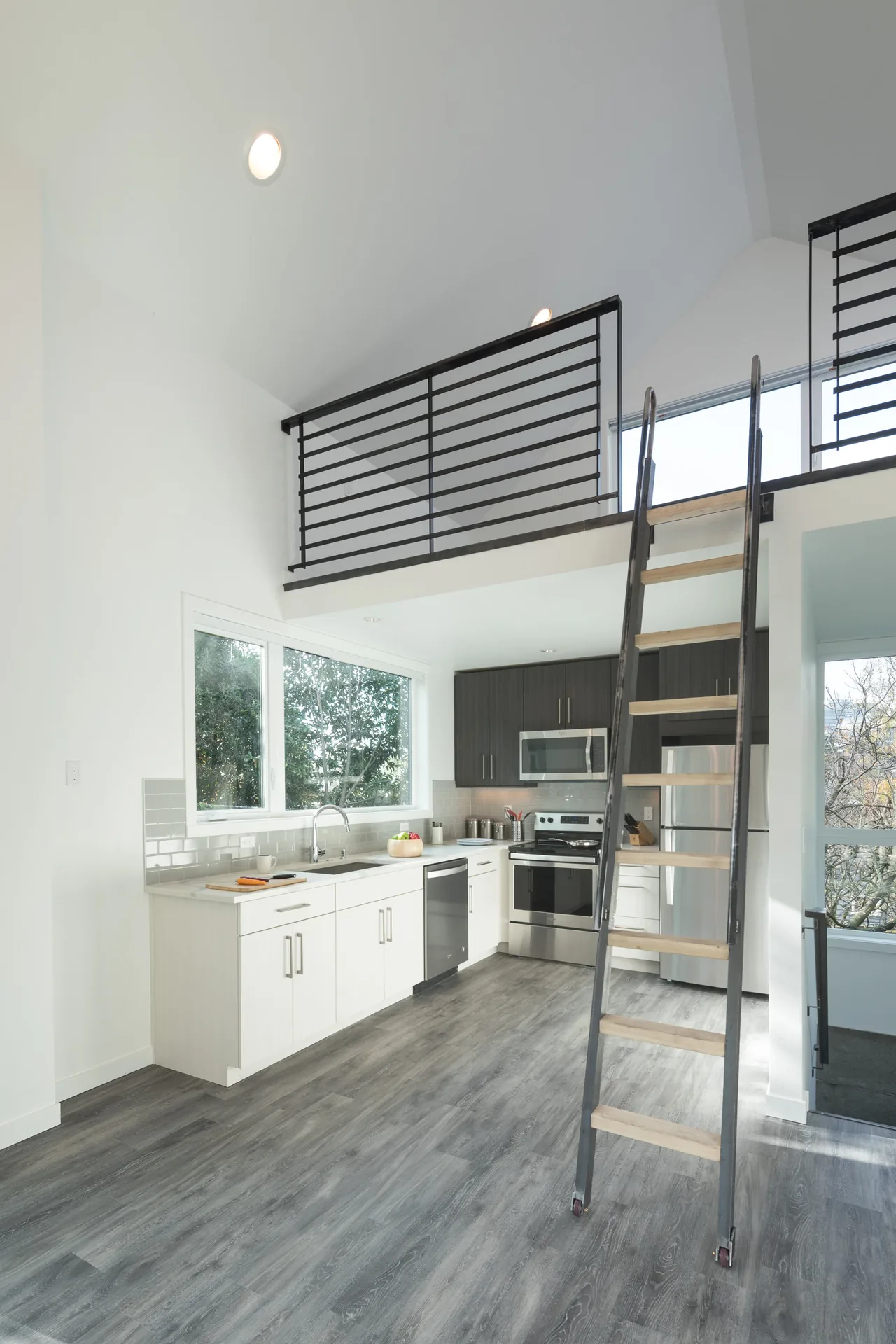 Kitchen features white and dark cabinetry, stainless steel appliances, and a ladder access to loft with metal railing.