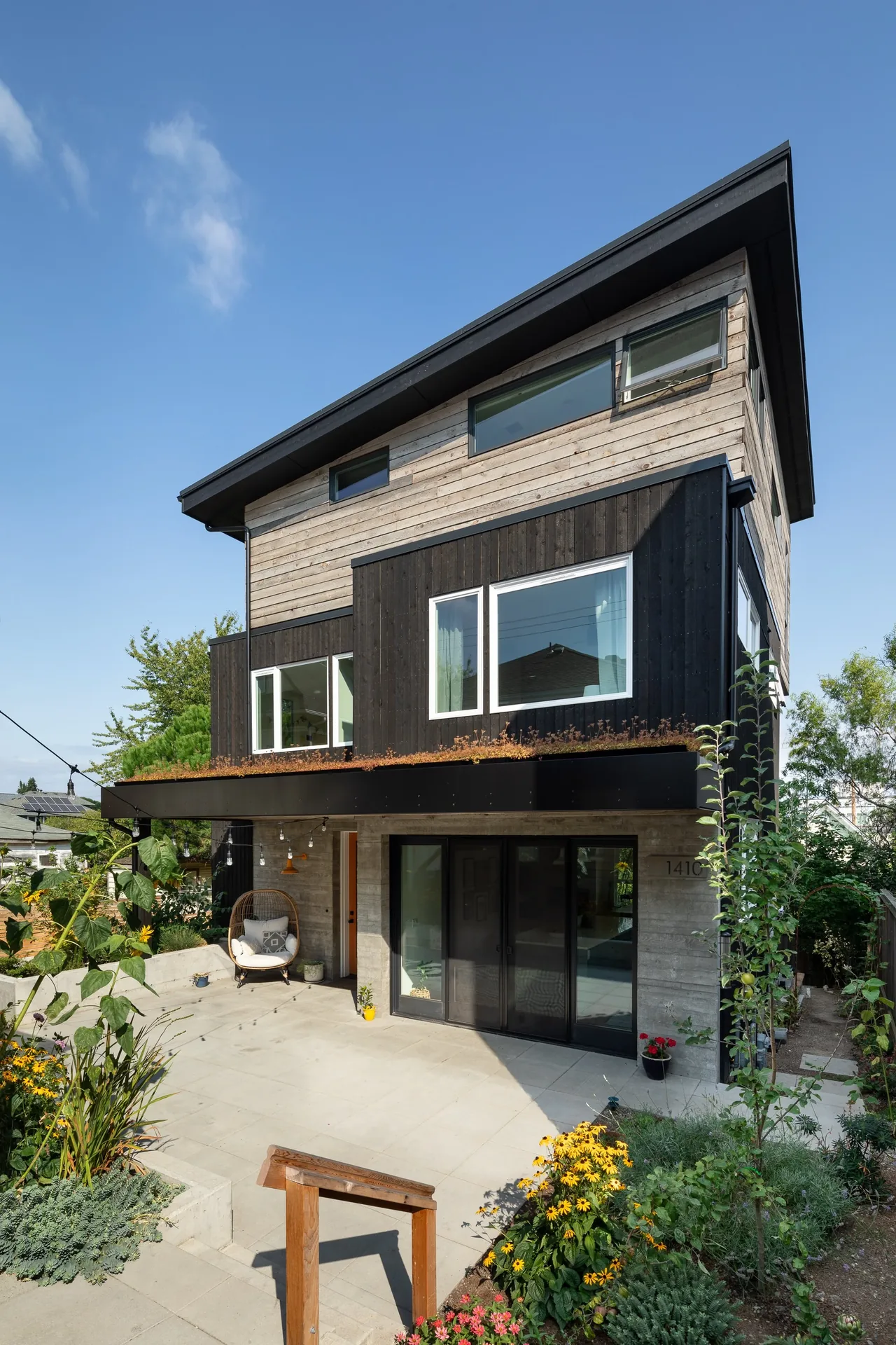 Backyard view of a modern two-story house with vertical wood siding and a sloped roof under a clear sky.