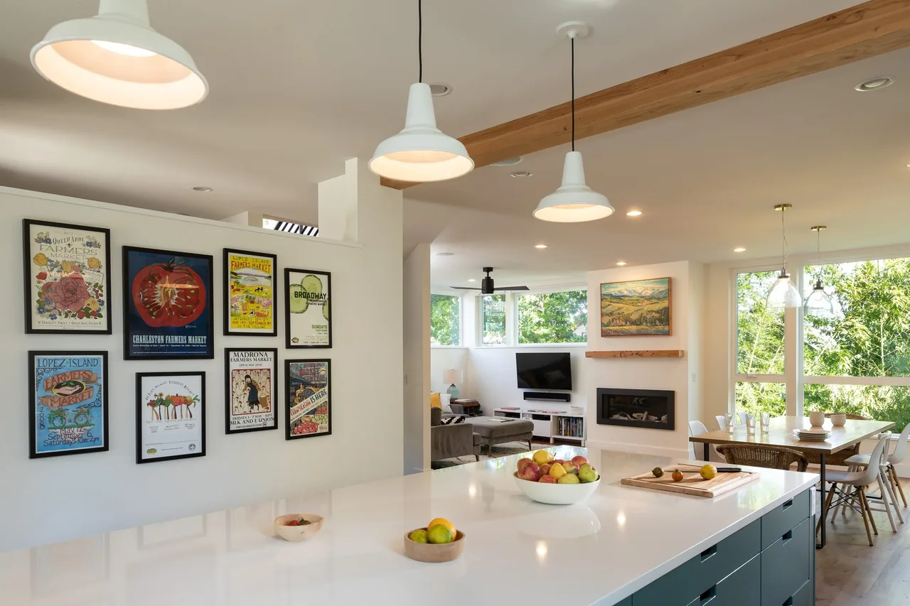 Open kitchen and living area with framed art on wall, modern pendant lights, and a dining table near large windows with views outside.