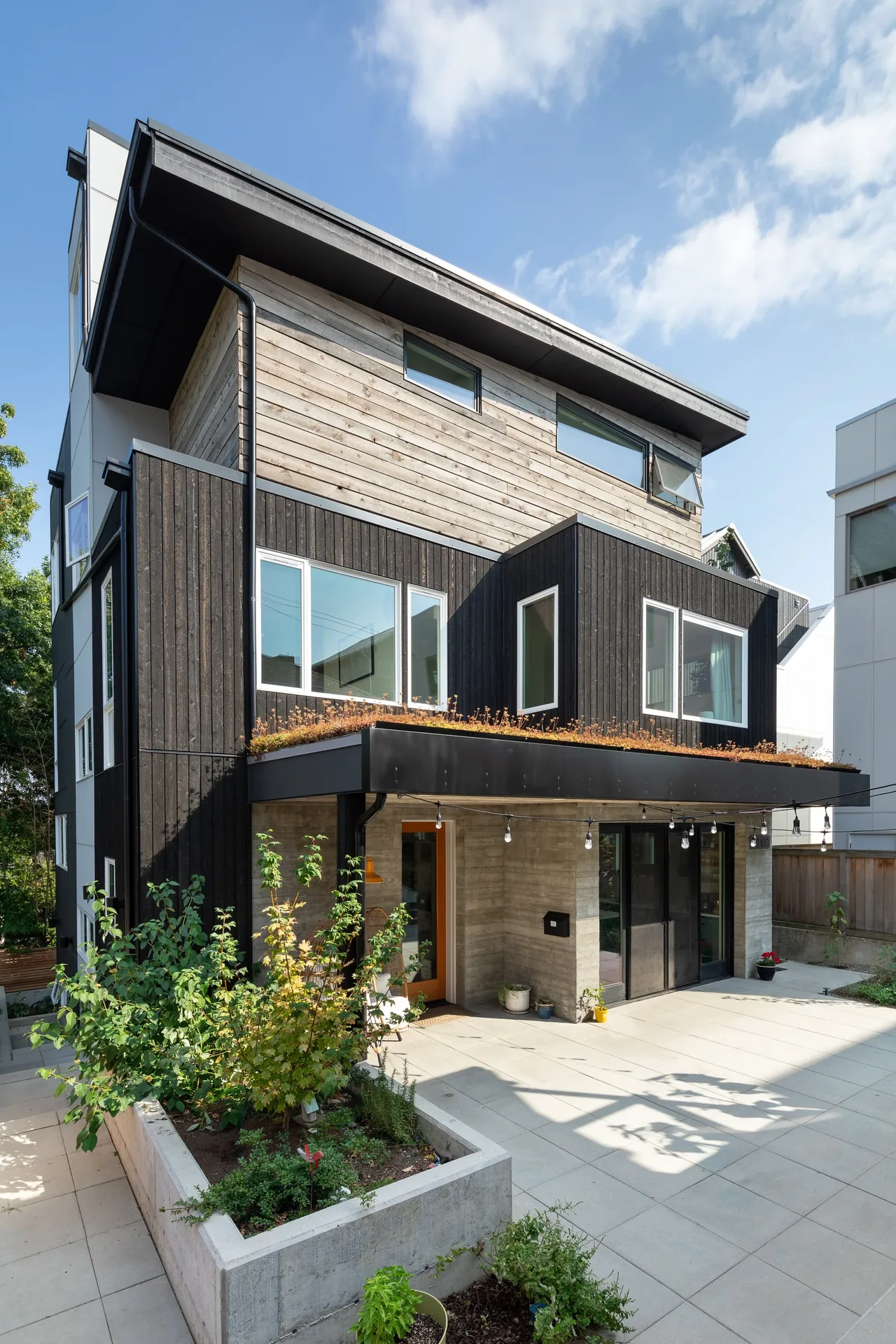 Backyard Residence by b9architects Inc. features wood siding, planted roof section, and large windows with black frames.