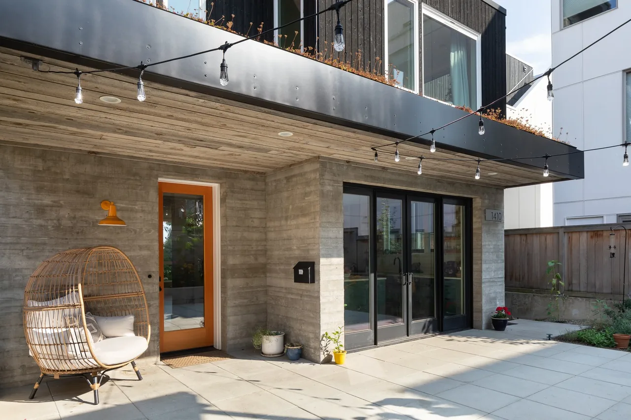Backyard Residence patio features board-formed concrete walls, string lights, and floor-to-ceiling glazing with black window frames.
