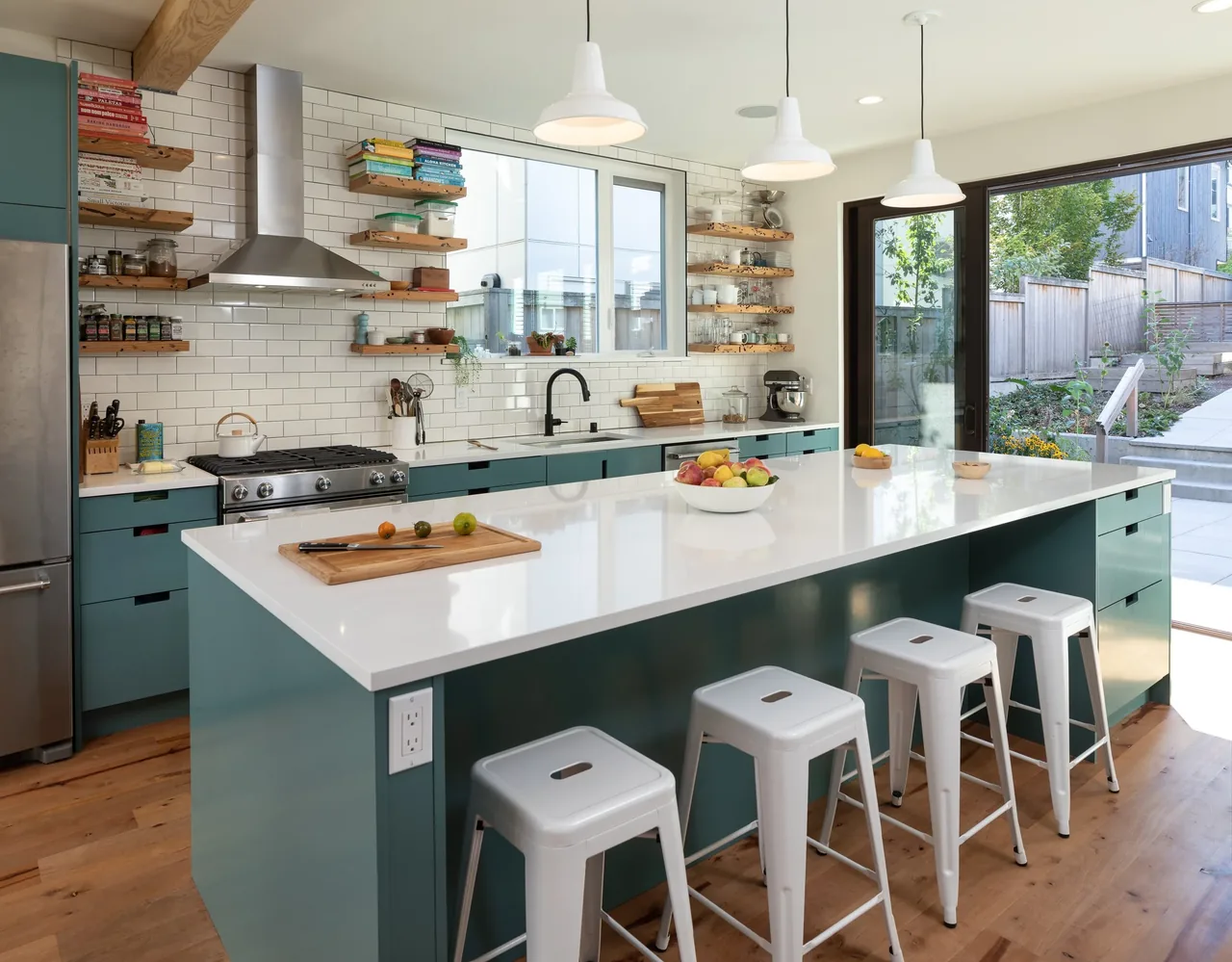 Kitchen features teal cabinetry, white subway tile backsplash, and a large island with white countertop and stools, opening to a patio.
