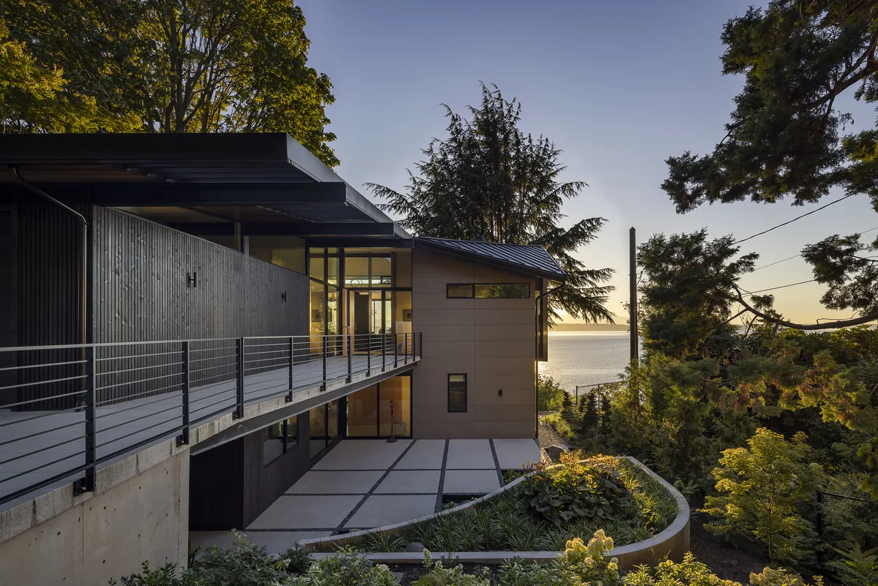 The modern exterior of Perkins Lane residence features a cantilevered balcony and large windows with a water view at sunset.