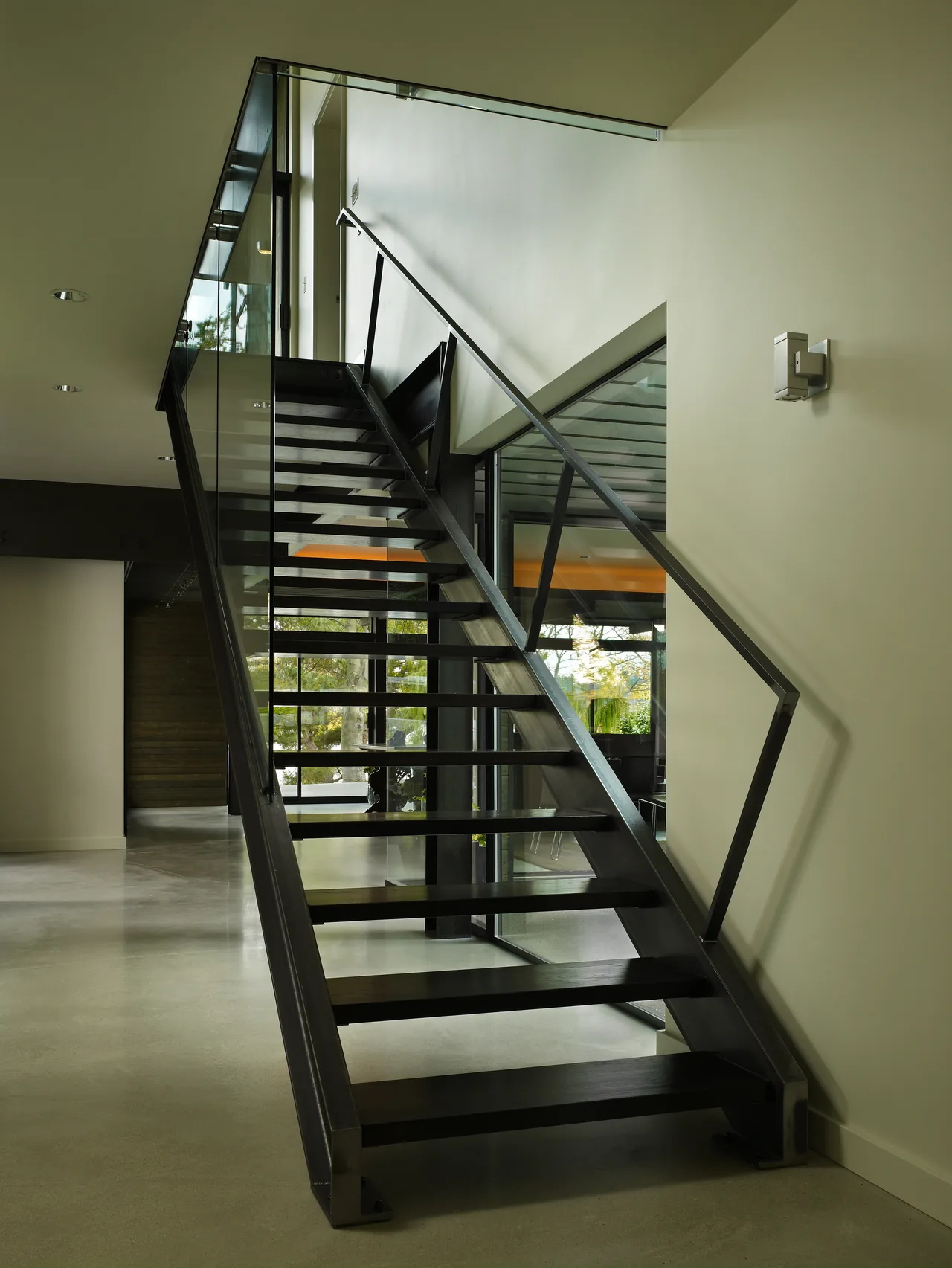 Interior view of a contemporary open-riser staircase with black metal framing and glass balustrade at Lake Washington Residence.
