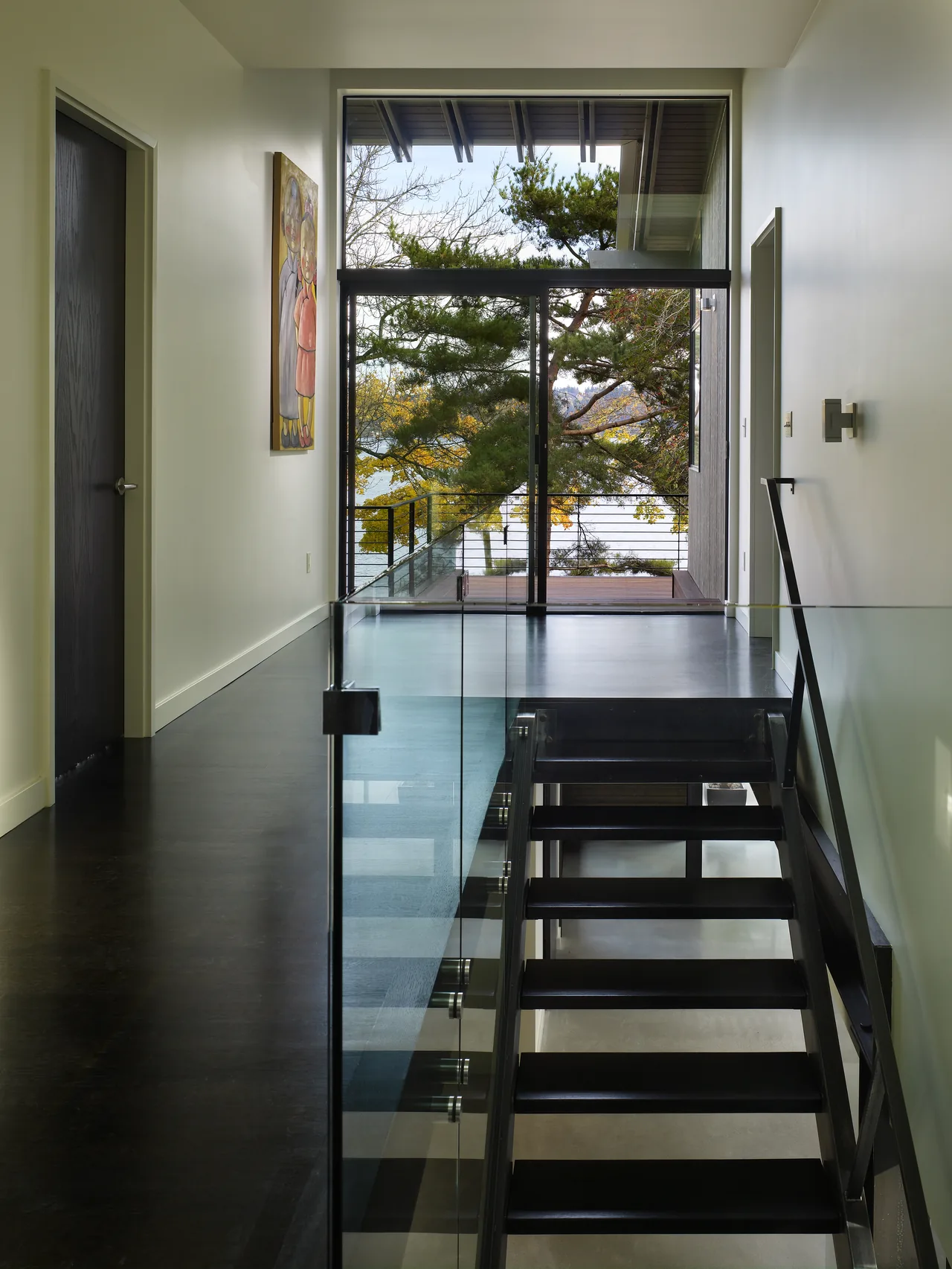 Hallway with modern black floating stairs and glass railing opens to a balcony with a view of Lake Washington.