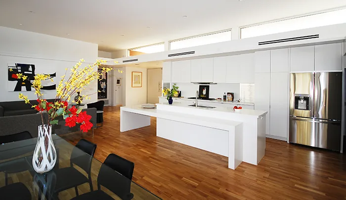 Minimalist kitchen and dining space with white cabinets, wood flooring, and clerestory windows in the Pulaski residence.