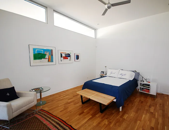 Bedroom with hardwood floors and high clerestory windows featuring abstract artwork above the bed.