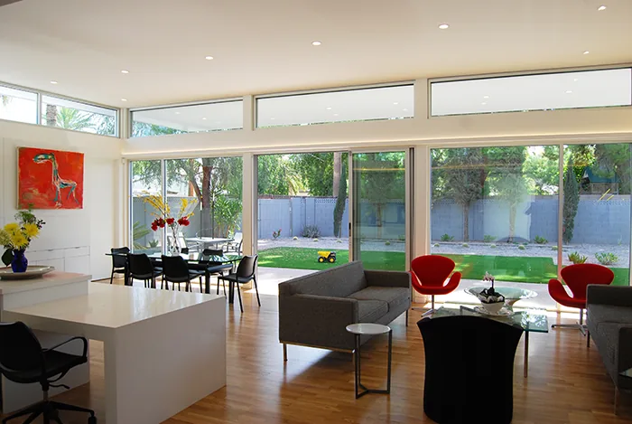 The living and dining area in the Pulaski residence features floor-to-ceiling sliding glass doors and clerestory windows, overlooking a green backyard.