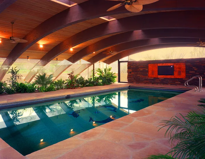 Klugness residence indoor pool area with curved wood-beam ceiling and planted border near floor-to-ceiling glazing.