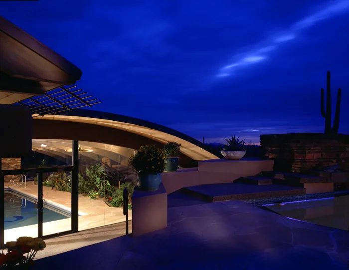 Curved roof and lit indoor pool area at dusk with a cactus silhouette in the background.