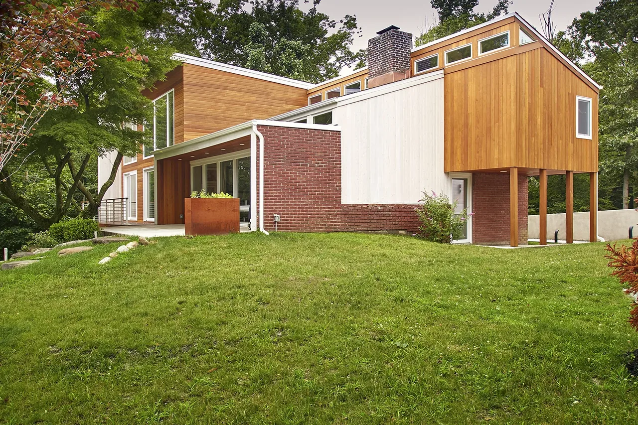 Mid-century to modern renovated house with two-tone wood and brick facade on a grassy slope.