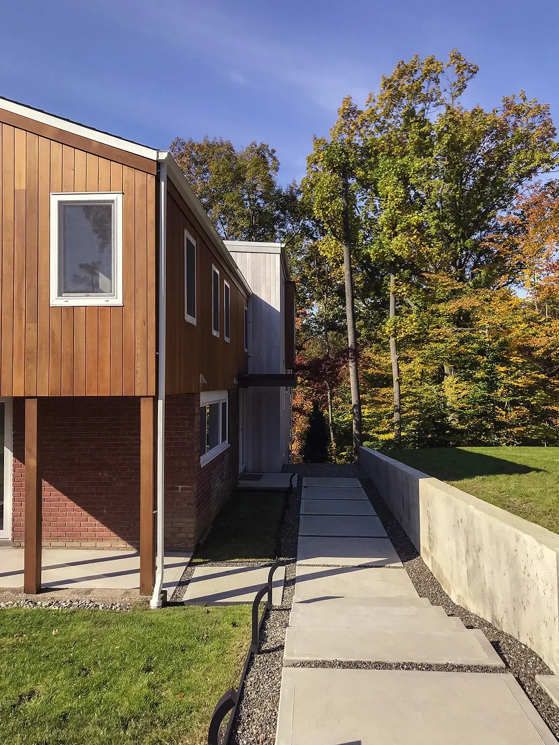 Side exterior of a mid-century to modern renovated house with two-tone facade, rectangular windows, and landscaped grassy slope.