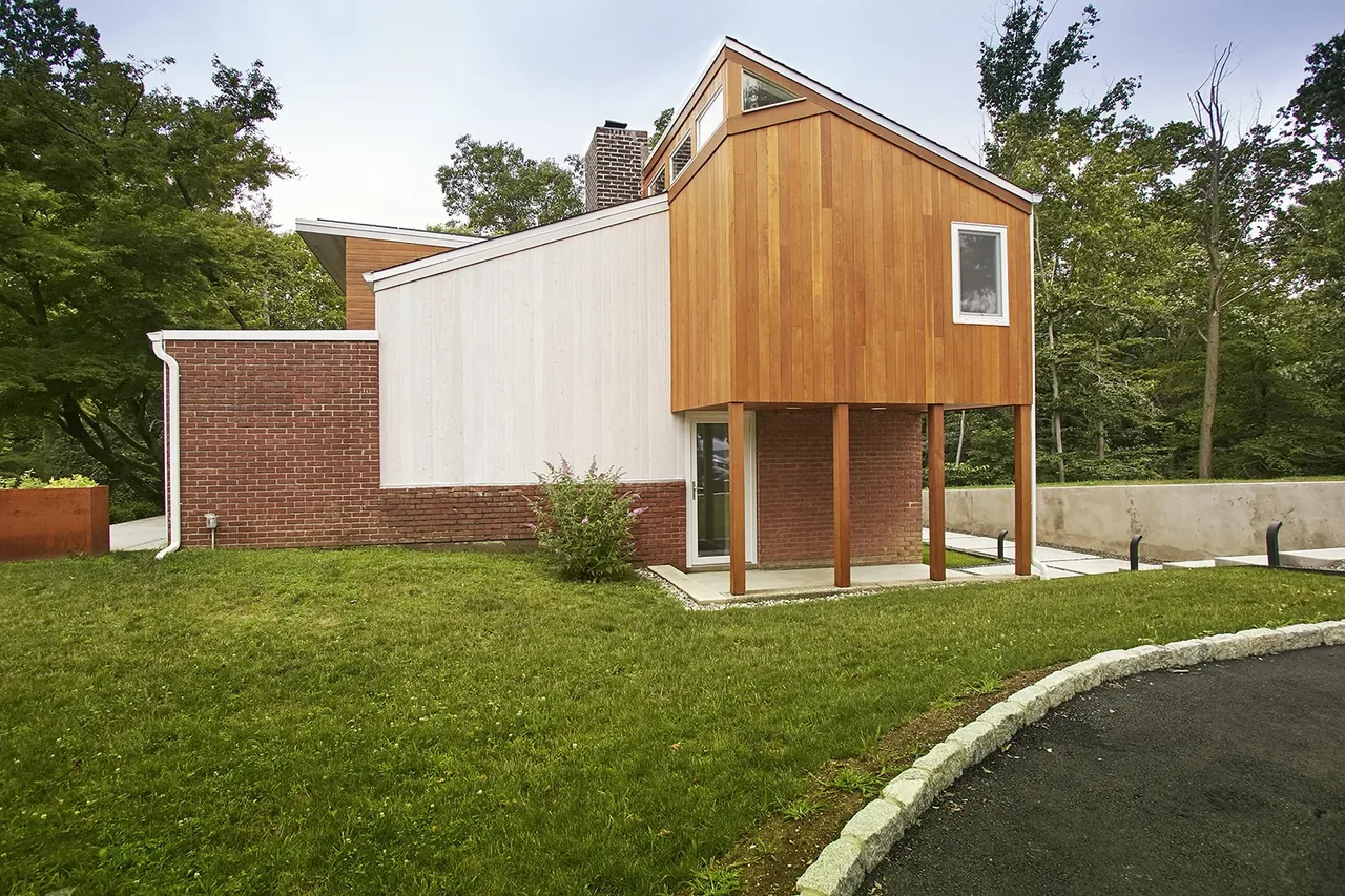 Mid-century to modern renovated house with red brick, two-tone white and wood siding, and a grassy slope in the front yard.