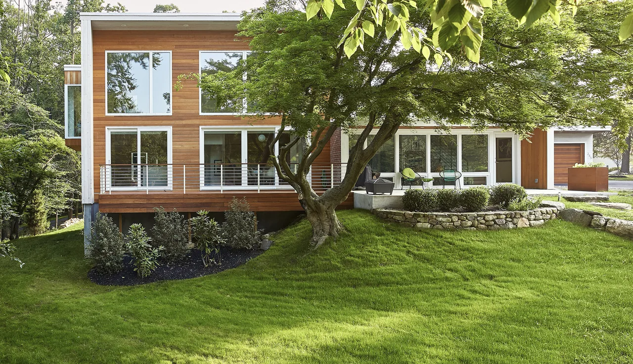 The Scoppettone/Leach House renovation features large window walls, wood siding, and a landscaped yard with stone retaining walls.
