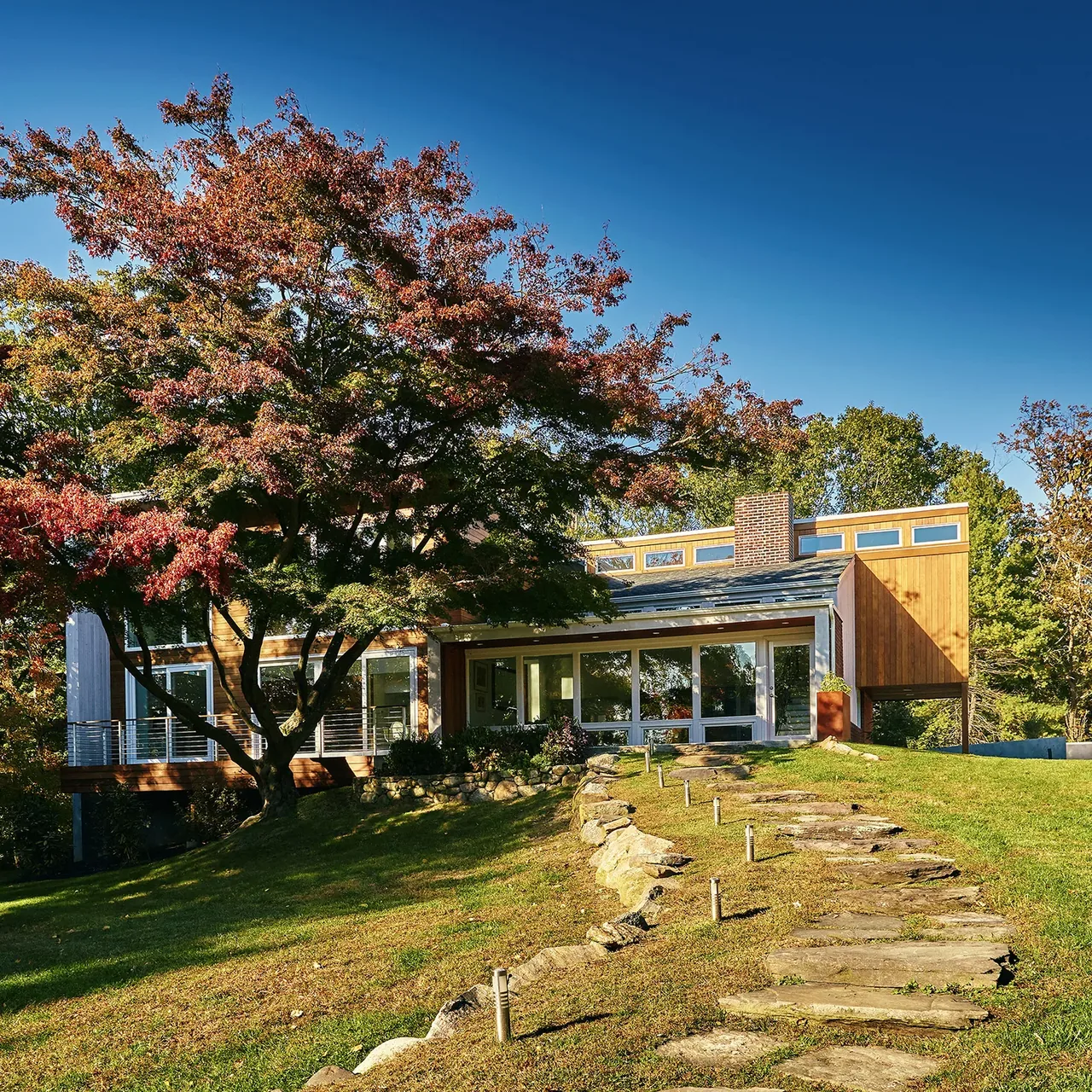 The Scoppettone/Leach House features a two-tone facade and rectangular windows, set on a sloped grassy yard with stone steps.