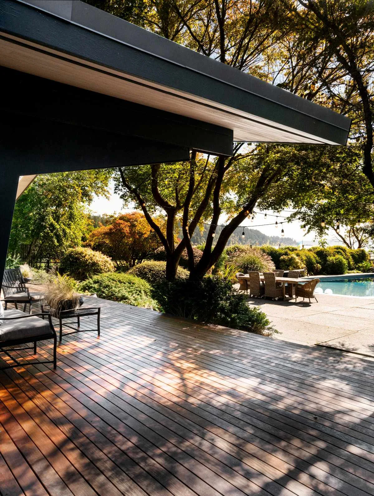 Outdoor living space featuring a wooden deck, garden landscaping, and poolside dining table.