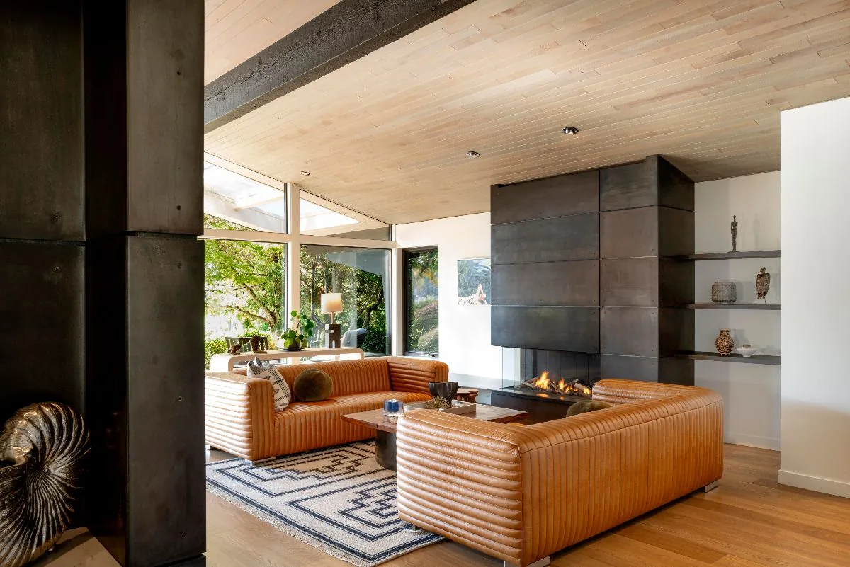 Mid-century style living room features leather sofas, a metal fireplace, and wood ceilings with large windows.