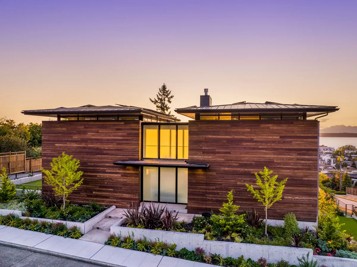 West Seattle House front exterior with wood siding, metal roofs, and concrete retaining walls under sunset lighting.