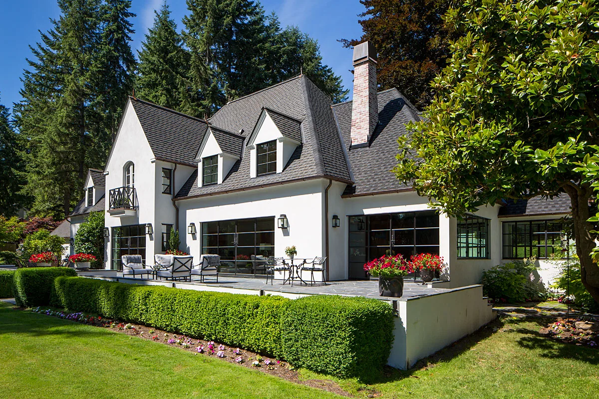 The Manzanita Bay House features a white stucco exterior with multiple steep gable roofs and black window frames overlooking a landscaped patio.
