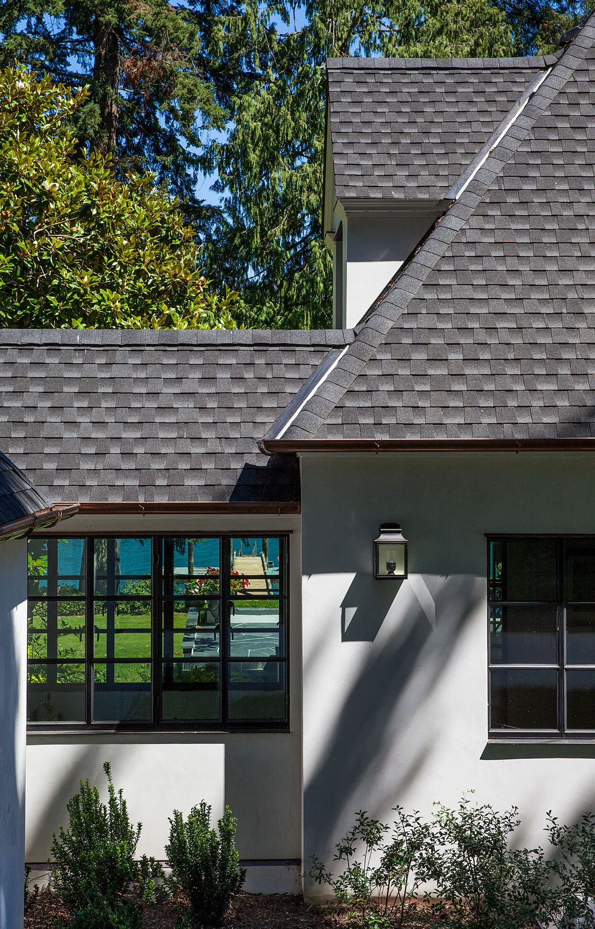 Manzanita Bay House exterior features dark shingle roofing, black window frames, and landscaped greenery.