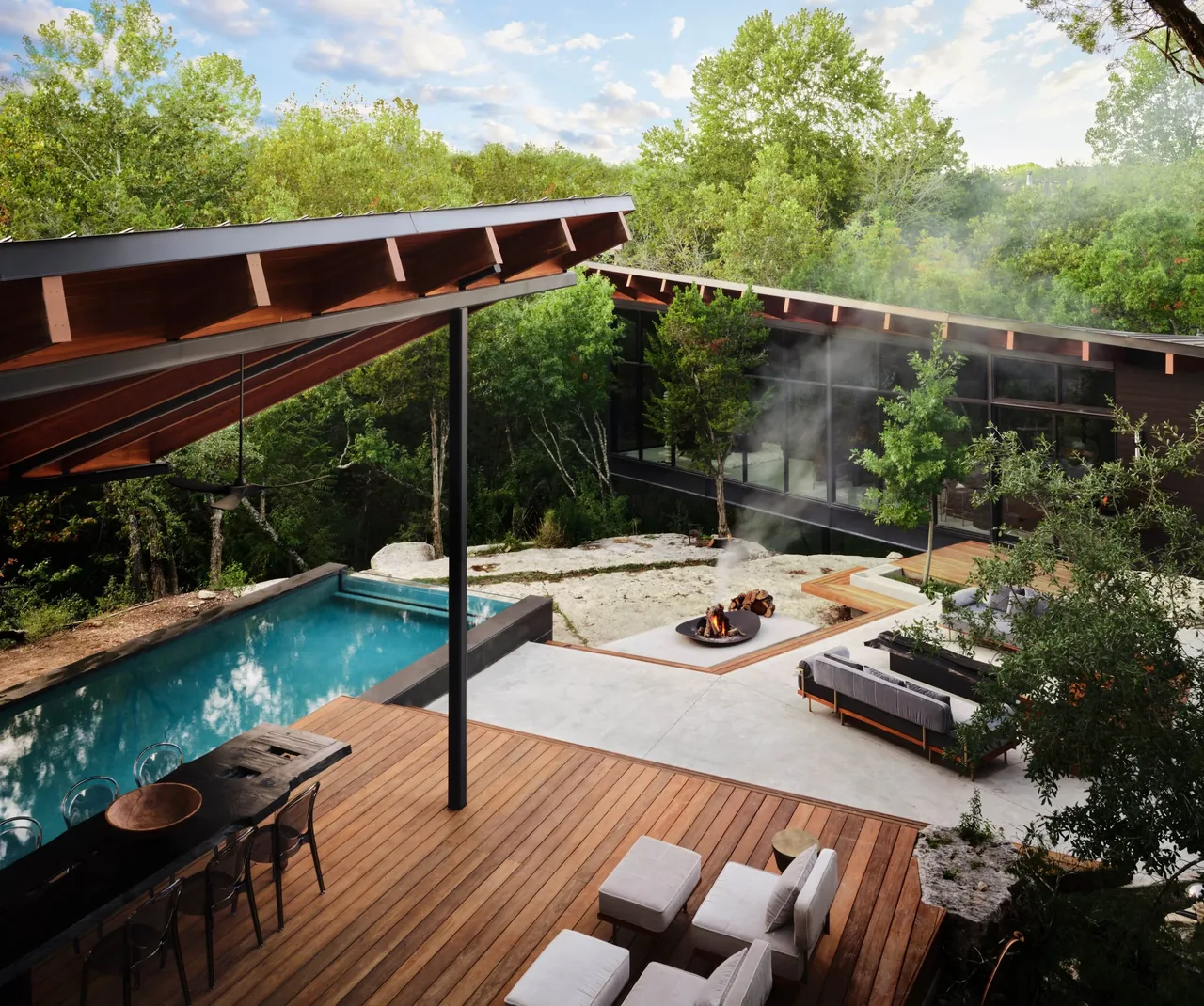 Falling Leaves House features an outdoor living area with a wooden deck, pool, and fire pit surrounded by greenery.