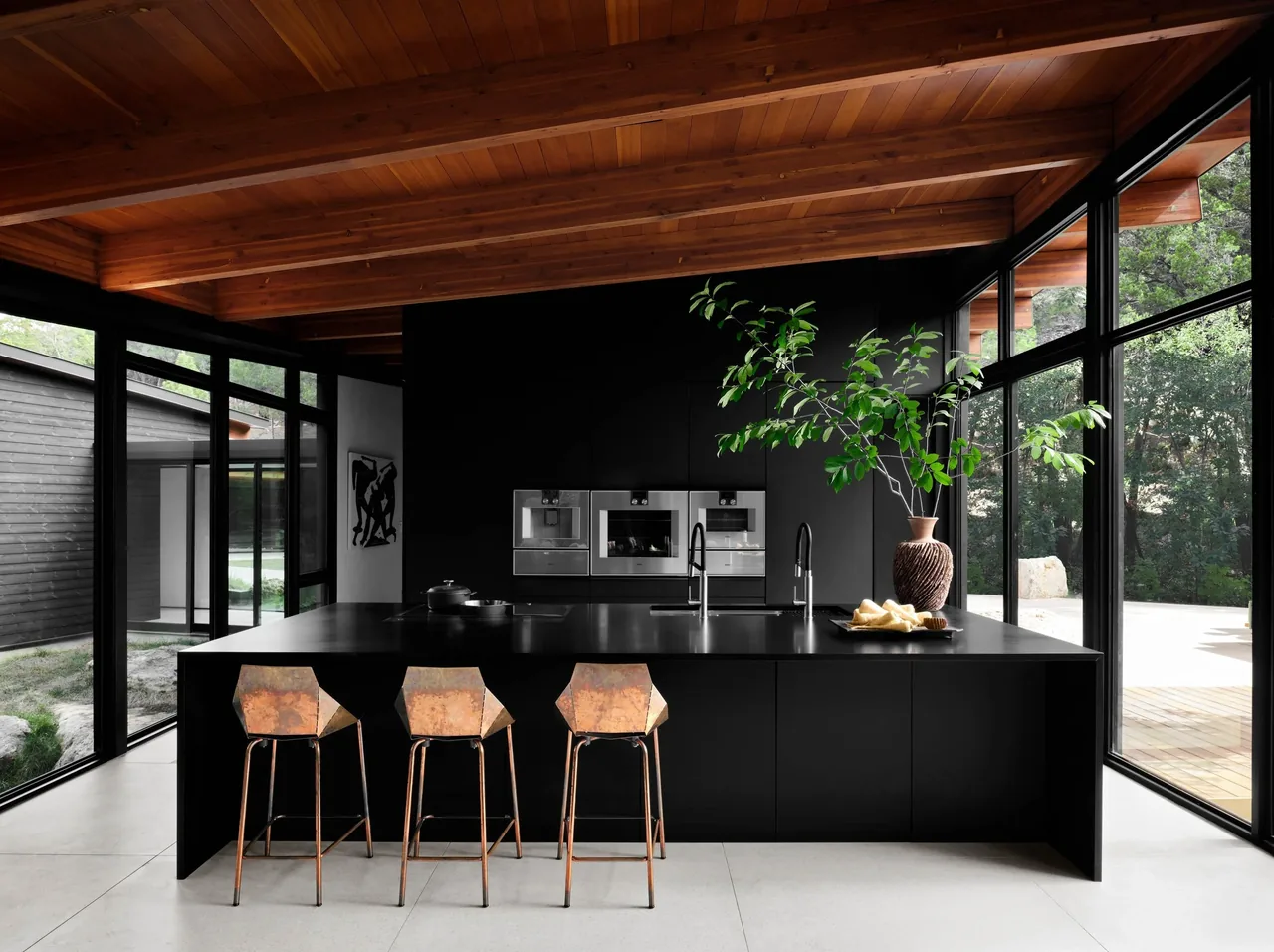 The Falling Leaves House kitchen features a black island with metal stools and a wood sloped ceiling with exposed beams.