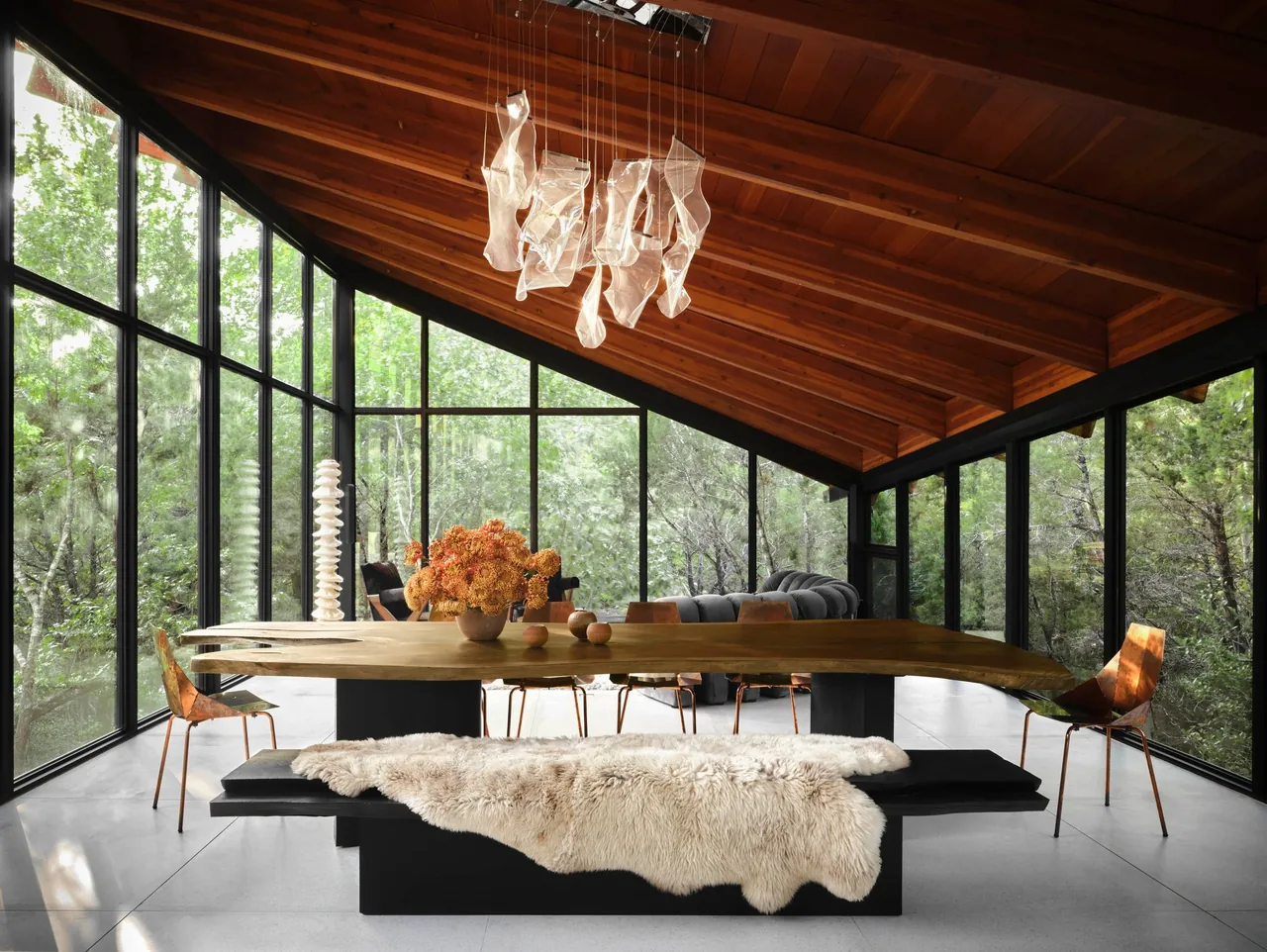 Dining room in the Falling Leaves House featuring floor-to-ceiling black-framed windows and a sloped wood ceiling.