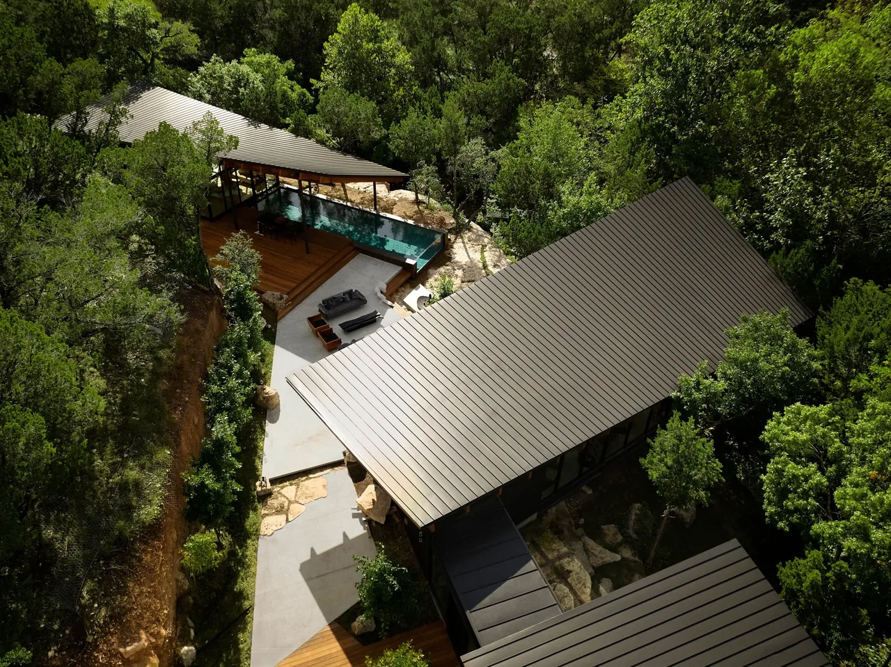 Falling Leaves House features elevated metal roof structures integrated into a wooded, rocky site.