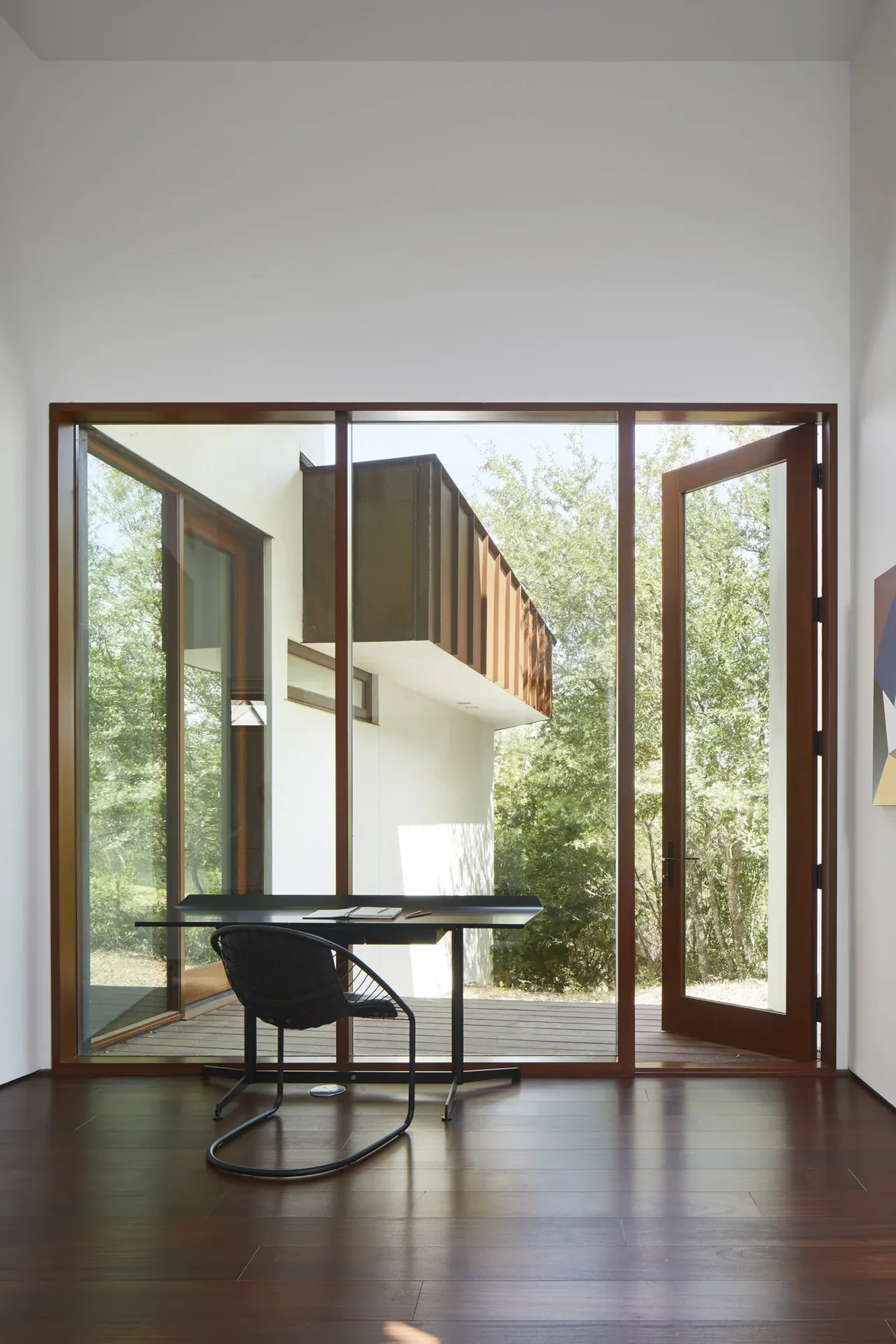 The Bold Ruler House office features a glass door and floor-to-ceiling windows opening to an outdoor deck with rust metal siding above.