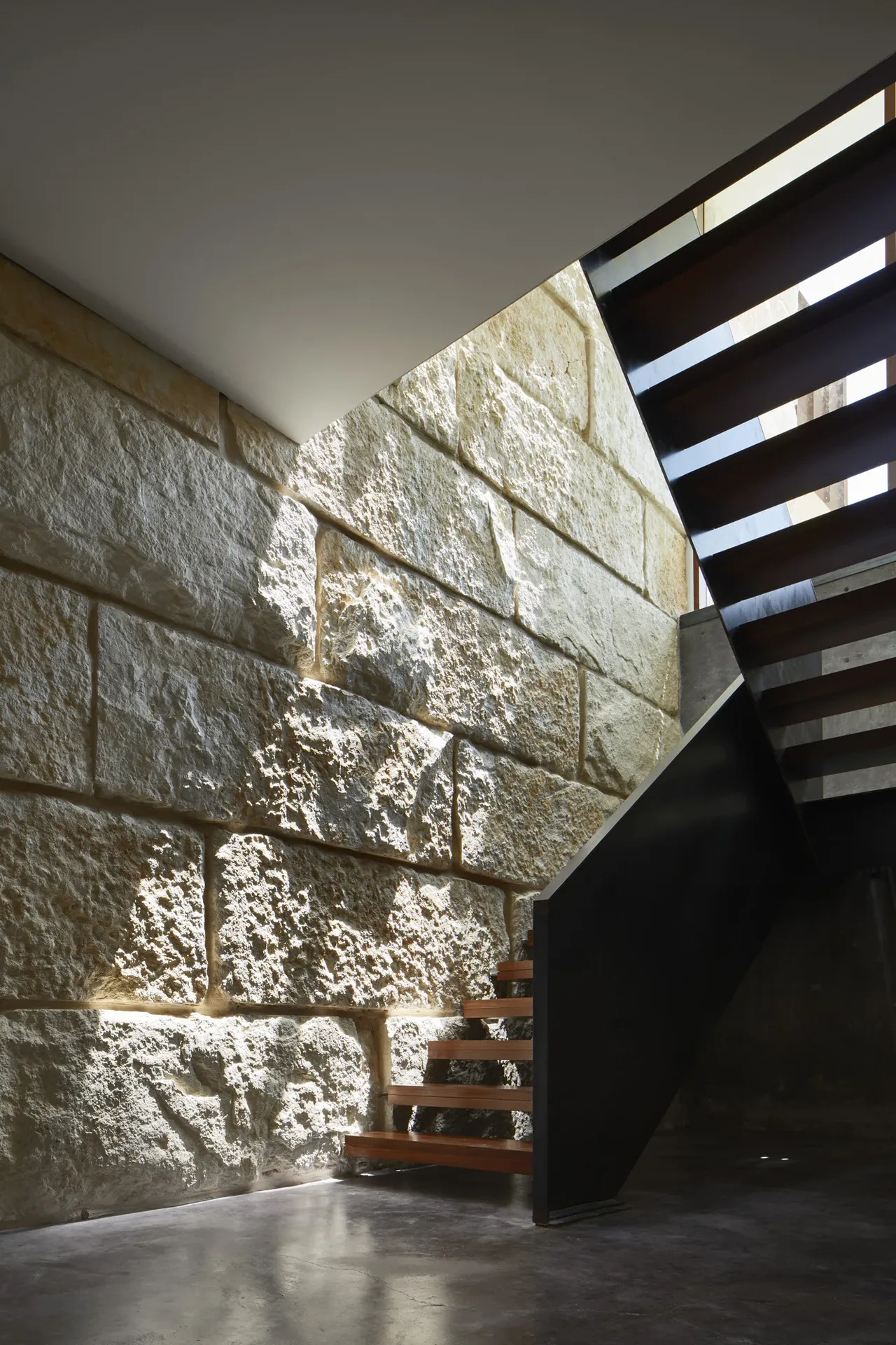 Modern staircase features exposed stone walls and floating wooden steps with metal supports.