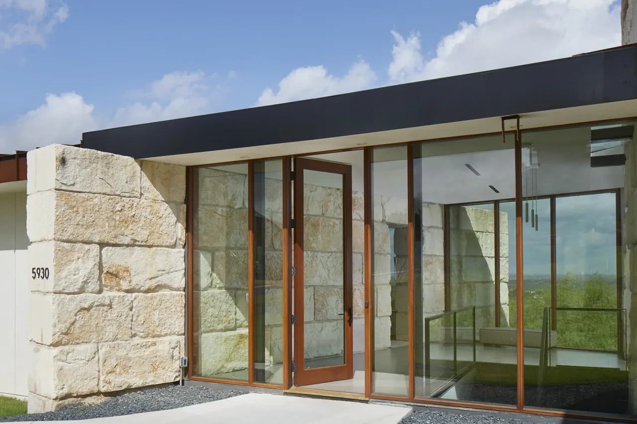 The Bold Ruler House entry features floor-to-ceiling glass doors with wood frames and a textured stone wall.